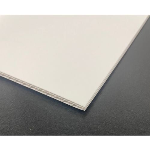 A close-up of the edge of a white "notFOAM 2.0 ARCHIVAL 11/64" Thick Plain Biodegradable Mounting Board" with visible corrugated layers, placed on a dark surface.