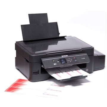 A black Epson printer actively printing Custom Image Strips, with several completed strips featuring red and black text visible on the output tray and surrounding workspace.