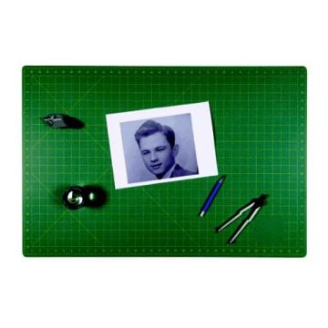 A SpeedPress 35.8" x 71.7" Magic Self-Healing Cutting Mat with a printed grid design, featuring drafting tools, a magnifying lens, and a black-and-white photograph placed on its surface.