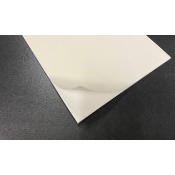 A close-up view of a white "notFOAM 2.0 ARCHIVAL 11/64" Thick Self-Adhesive Biodegradable Mounting Board" with a corner slightly peeling back, placed on a textured dark surface.