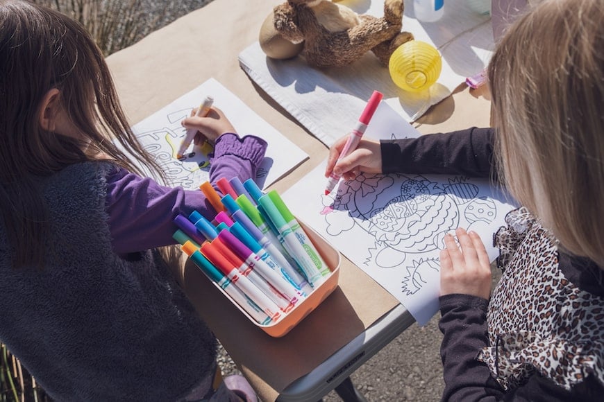 Two young girls using colored markers to fill in drawings.