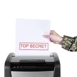A person in military camouflage uniform feeds a sheet labeled "TOP SECRET" into a paper shredder, representing secure document disposal as part of Military Office Supplies.